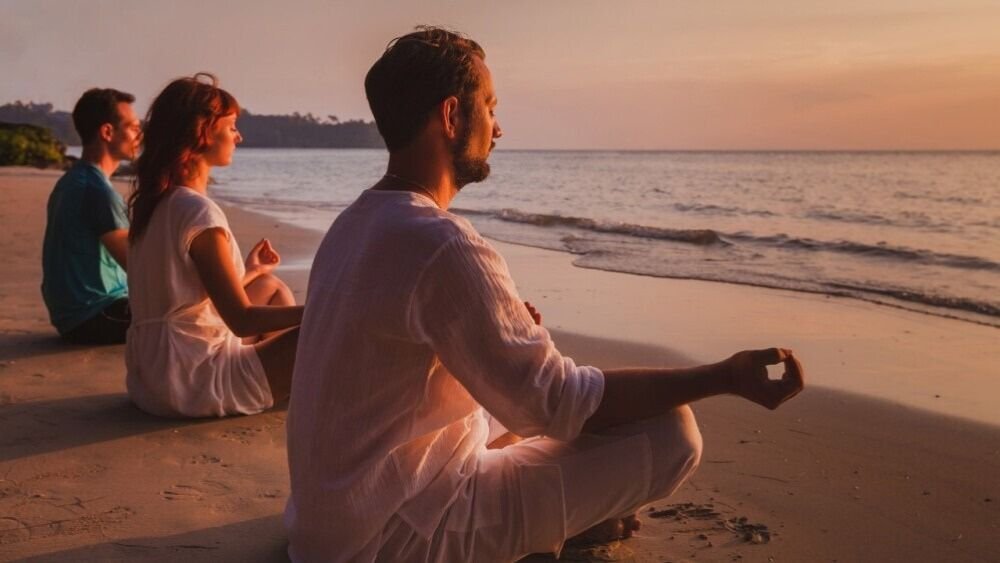 People meditating on a beach at sunset, practicing mindfulness and relaxation by the ocean.
