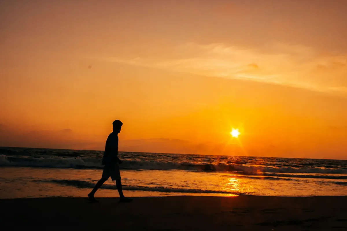 Silhouette of a person walking on a beach at sunset, representing high emotional frequency, mental clarity, and the expansion of personal possibilities in life and finance.