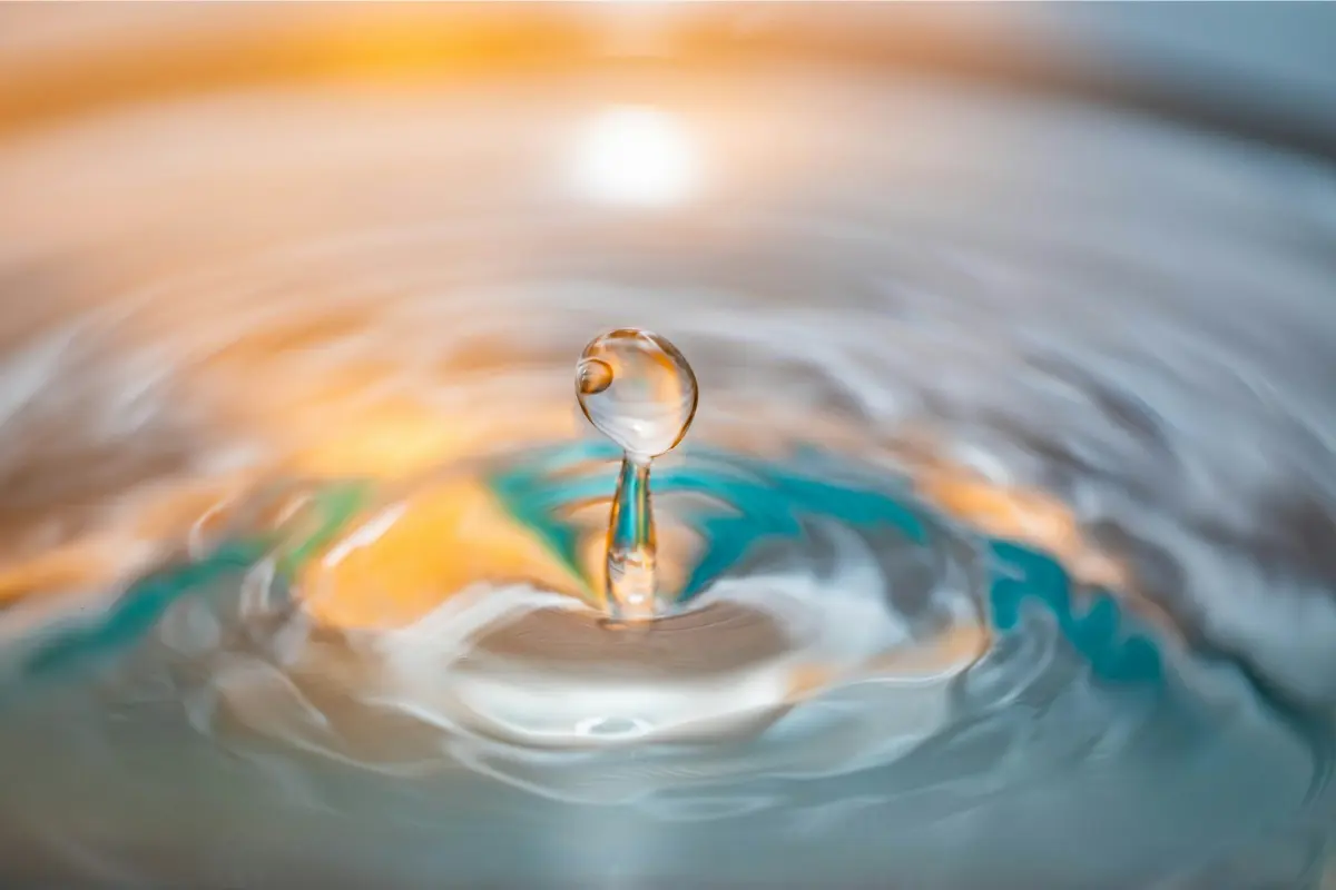 A minimalist macro shot of a golden water droplet creating clear ripples on a serene blue surface, symbolizing the micro-shift principle of how to raise your vibration with a 5-minute reset.